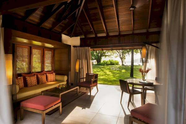 Innenansicht des Wohnbereichs im Constance Ephelia Resort mit Couch, Tisch, Stühlen und Ausblick auf Rasen.