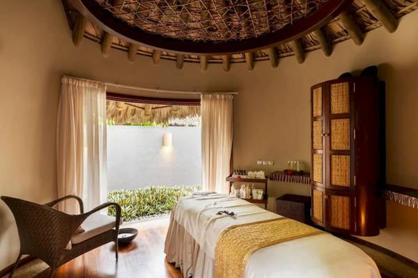Massage-Raum im Constance Ephelia Resort mit Behandlungstisch, Fenster und üppigem Dekor.