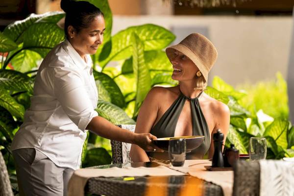 Mitarbeiterin des Constance Ephelia Resorts lächelt eine Gast mit einem Essen an.