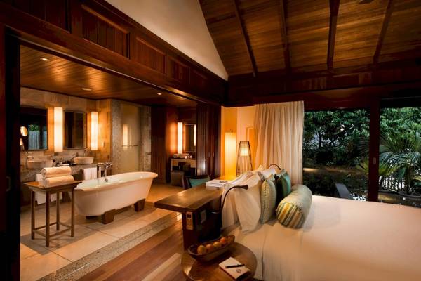 Innenansicht eines Luxus-Schlafzimmers im Constance Ephelia Resort mit Badewanne, Bett und offenem Fenster.