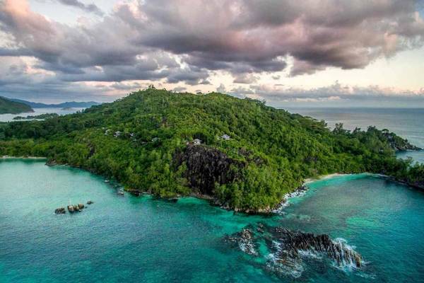 Aussicht auf das Constance Ephelia Resort auf einer kleinen Insel mit dichtem Grün und türkisfarbenem Wasser.