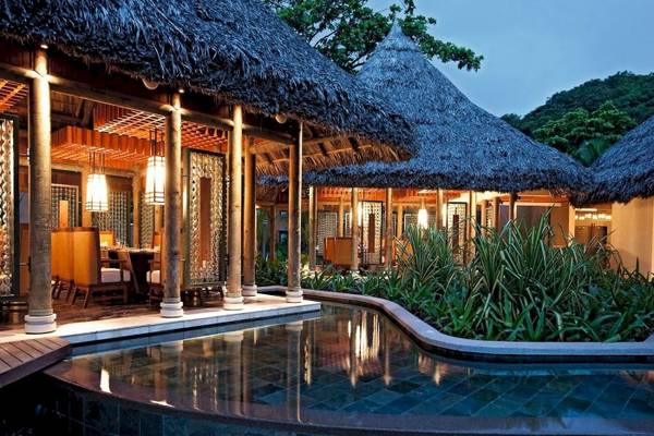 Außenbereich des Constance Ephelia Resorts mit Swimmingpool und traditionellen Strohdächern