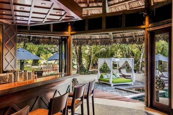 Innenansicht der Bar und Loungebereich des Constance Ephelia Resorts mit grüner Bettlandschaft und Sonnenschirmen.