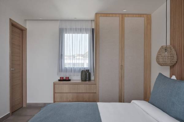 Inneneinrichtung eines Schlafzimmers im Atlantica Beach Resort Kos mit Doppelbett, Nachttisch, Kleiderschrank und Fenster mit Vorhängen.