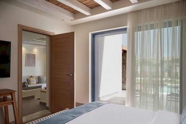 Innenansicht eines Zimmers im Atlantica Beach Resort Kos mit offenem Eingang, offenem Balkon, Bett, Fernseher und Blick auf den Pool.