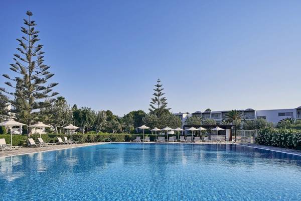 Außenpoolbereich des Atlantica Beach Resort Kos mit weißen Liegestühlen und Sonnenschirmen.
