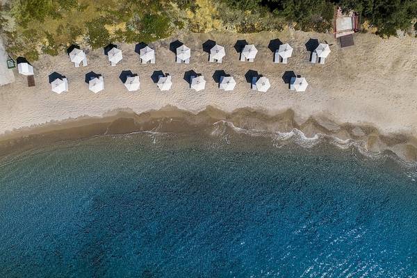 Luftaufnahme des Atlantica Beach Resort Kos mit vielen weißen Sonnenschirmen am Strand und blauem Meer.