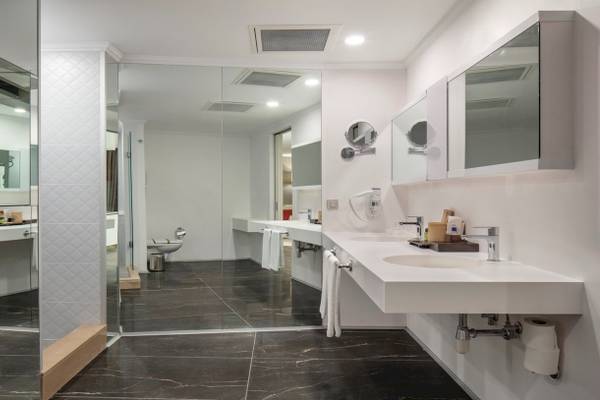 Das Badezimmer des Nirvana Cosmopolitan Hotels mit weißen Waschbecken und schwarzen Marmorboden.