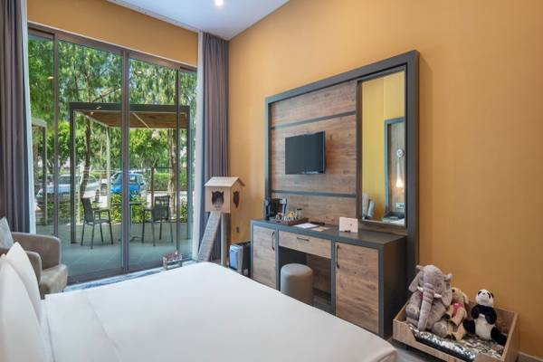 Ein Hotelzimmer im Nirvana Cosmopolitan mit Panoramafenstern, die auf einen Garten und eine Terrasse mit Tischen und Stühlen hinausführen.