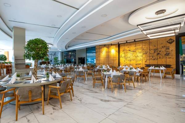 Innenbereich des Nirvana Cosmopolitan Hotels mit gerundeten Tischen, Holzstühlen und weißer Marmorfliesen.