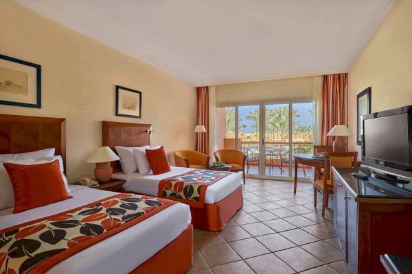 Innenansicht eines Doppelzimmers im Jaz Grand Marsa Hotel mit zwei Betten, Fernseher und Balkon.