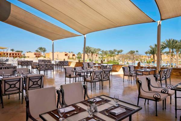 Außenbereich des Jaz Grand Marsa Hotels mit Tisch und Stühlen unter Sonnenschirmen.