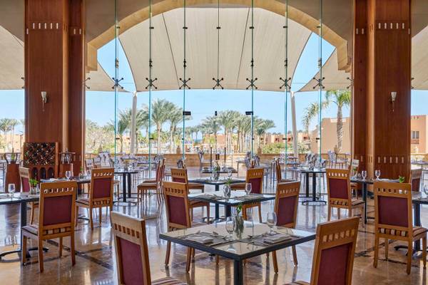 Restaurantbereich im Jaz Grand Marsa Hotel mit Glaswänden und Blick auf Palmen.