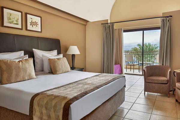 Doppelzimmer im Jaz Lamaya Resort mit Bett, Kissen, Nachttisch, Lampe und Balkon.