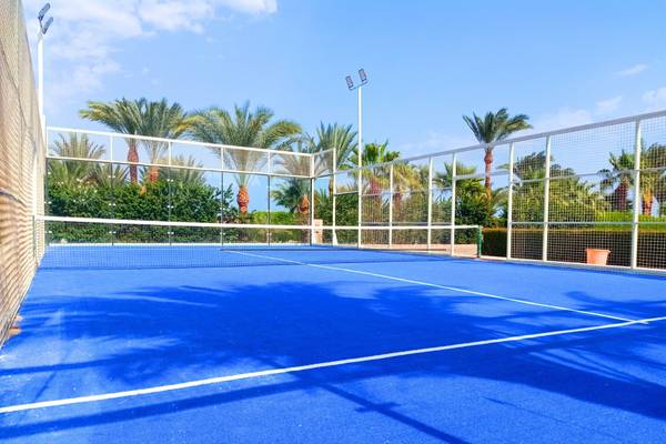 Ein leerer Tennisplatz des Utopia Beach Club mit blauem Boden und hohen Palmen im Hintergrund.