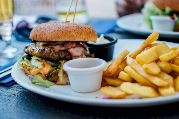 Ein Burger mit Pommes Frites auf einem weißen Teller, serviert mit einer Tasse Ketchup.