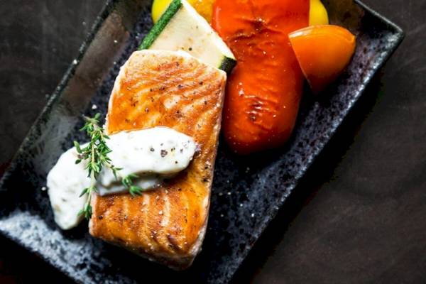 Gegrillter Lachs mit Gemüse und Kräutern auf einem schwarzen Teller.