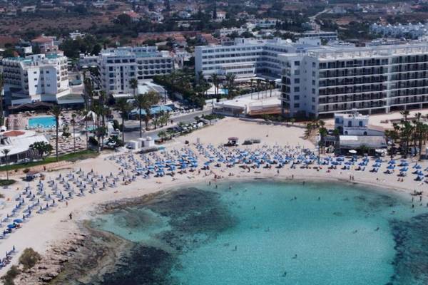 Luftaufnahme des Anonymous Beach Hotels mit vielen Gästen und blauen Sonnenschirmen am Strand.