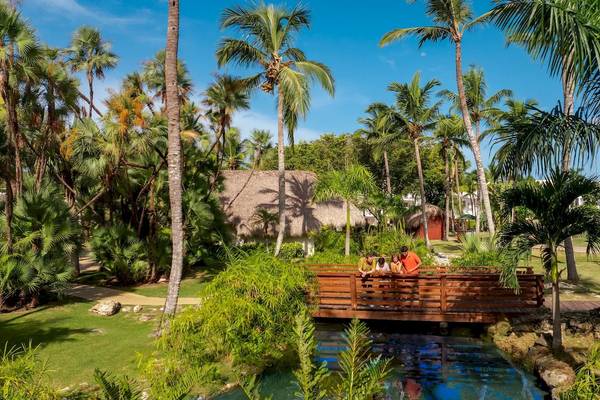 Familie auf einer Brücke im Sunscape Dominicus La Romana Hotel, umgeben von Palmen und Wasser.