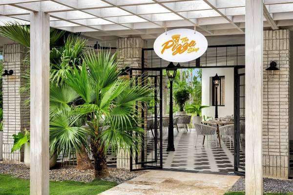 Eingang zum Hotel-Restaurant mit Palmenbaum und schwarzen Gittertüren.