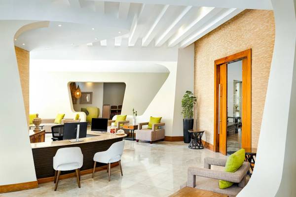Innenraum des Hotels Sunscape Dominicus La Romana mit Rezeptionstresen, weißen Stühlen und grünen Kissen.