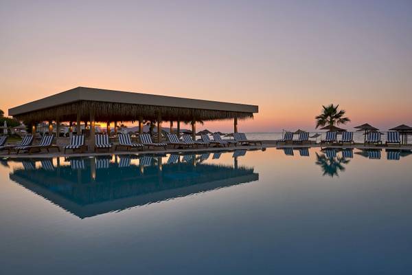 Atlantica Kalliston Resort Pool bei Sonnenuntergang mit Liegen und Sonnenschirmen