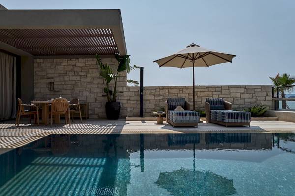 Terrasse des Atlantica Kalliston Resorts mit Sonnenschirm und Sesseln neben einem Pool.