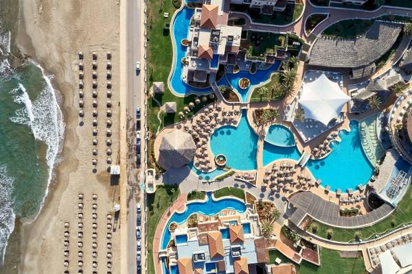 Luftaufnahme des Außenbereichs des Atlantica Kalliston Resorts mit mehreren Swimmingpools und Sonnenschirmen.