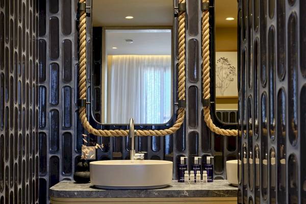 Badezimmer des Atlantica Kalliston Resorts mit schwarzer Fliesenwand und Spiegeln, die mit Seilen verziert sind.