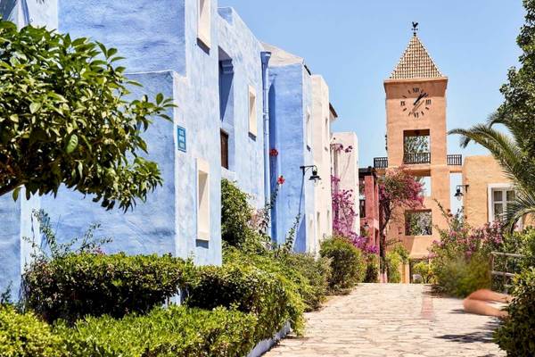 Haupteingang des Candia Park Village Hotels mit blauen Gebäuden und einer Uhrturm im Hintergrund.