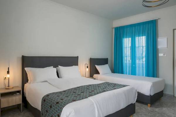 Zweibettzimmer im Corissia Beach Hotel mit weißen Wänden, zwei Betten und blauen Vorhängen.