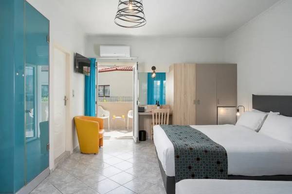 Innenansicht eines Zimmers im Corissia Beach Hotel mit zwei Betten, einem Schreibtisch, einer Klimaanlage und einem Balkon.