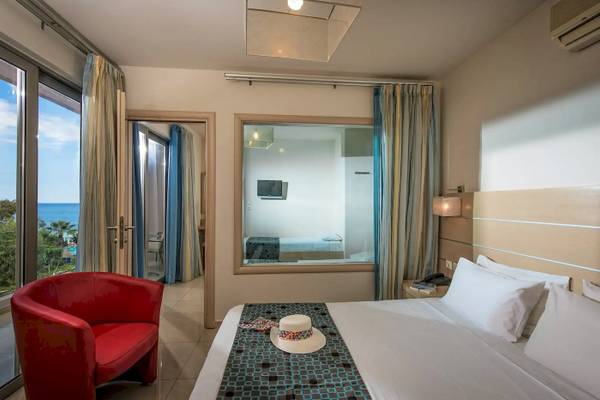 Innenansicht eines Zimmers im Corissia Beach Hotel mit Meerblick, einem großen Bett und einem roten Sessel.