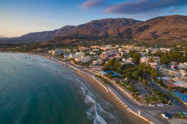 Luftaufnahme des Corissia Beach Hotels mit Strand, Gebäuden und Bergen im Hintergrund.