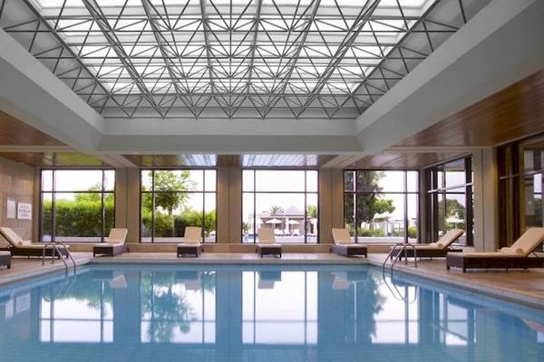 Innenpool im Sheraton Rhodes Resort mit Lounge-Liegestühlen und Glaswänden.