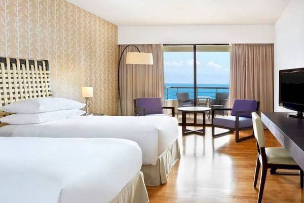 Hotelzimmer im Sheraton Rhodes Resort mit Blick auf den Ozean, drei Betten und einem Schreibtisch.