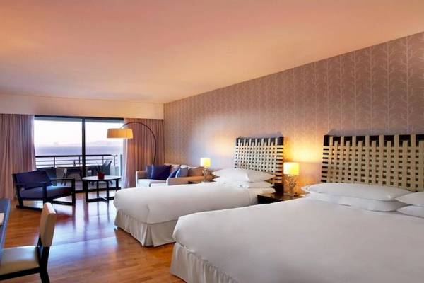 Doppelzimmer mit Meerblick im Sheraton Rhodes Resort mit zwei Betten, Schreibtisch, Sesseln, Couch, Fenstern und Balkon.