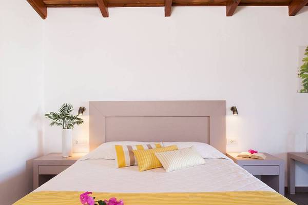 Schlafzimmer im Chrissi Amoudia Hotel mit gelben und weißen Bettwäsche, Blumen und Nachttischen.