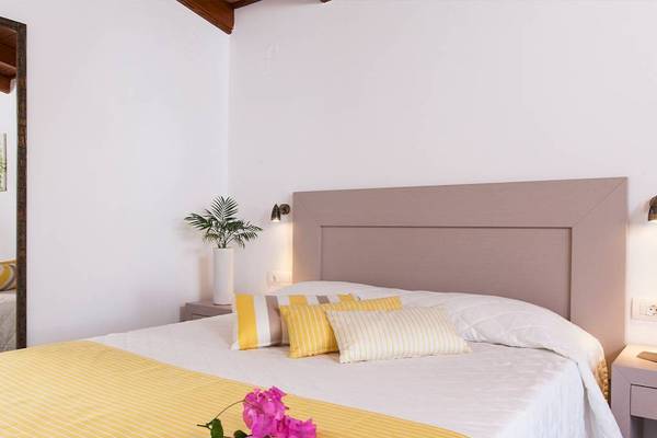 Schlafzimmer im Chrissi Amoudia Hotel mit weißen Wänden, gelben und weißen Kissen, und Blumen auf dem Bett.