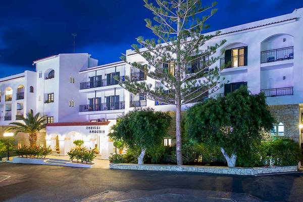 Die Außenansicht des Chrissi Amoudia Hotels bei Nacht mit einem großen Baum vor dem Gebäude.