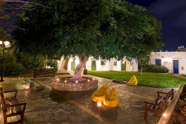 Chrissi Amoudia Hotel Atrium mit großer zentraler Baum, gelben Sitzsäcken und Nachtbeleuchtung.