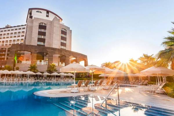 Melas Lara Hotel im Sonnenaufgang mit Swimmingpool und Sonnenschirmen.