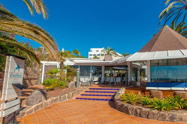 Außenbereich des Corallium Beach by Lopesan Hotels mit geometrischem Gebäude und blauen Sitzgelegenheiten.