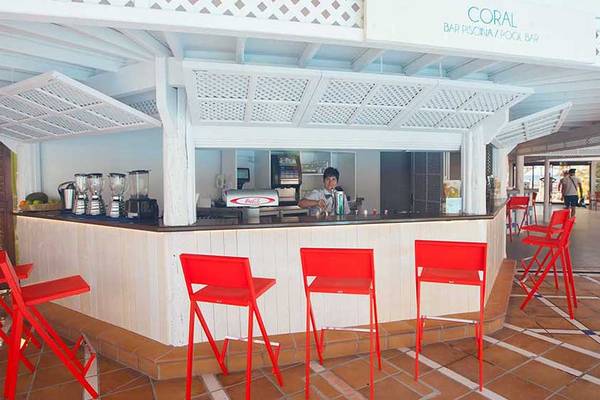 Innenansicht der Bar Corallium Beach by Lopesan Hotels mit roter Sitzgelegenheit und Barkeeper.