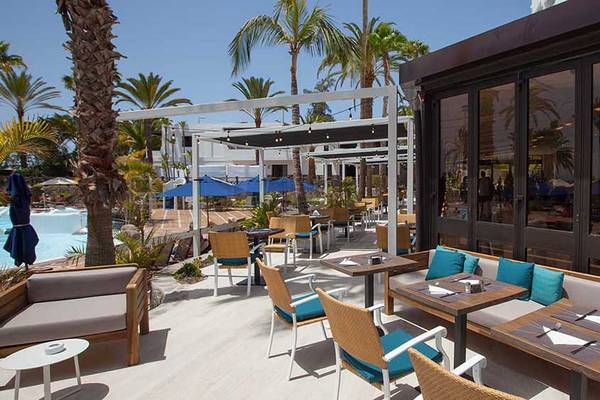 Terrasse des Corallium Beach by Lopesan Hotels mit Tischen, Stühlen und Sonnenschirmen.