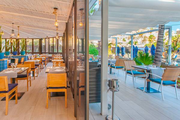 Innenansicht des Restaurants Corallium Beach by Lopesan Hotels mit blauen Tischen und Stühlen.