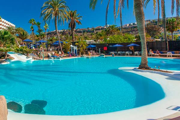 Außenpoolbereich des Corallium Beach Hotels von Lopesan Hotels mit Wasserrutsche und Sonnenliegen.