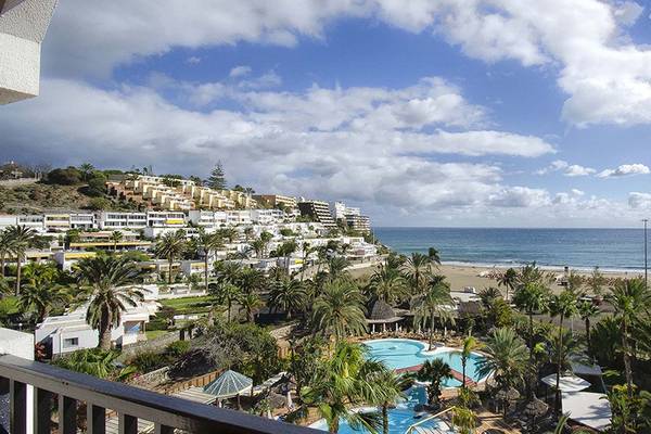 Aussicht vom Balkon des Corallium Beach by Lopesan Hotels auf den Strand, die Palmen und das Meer.