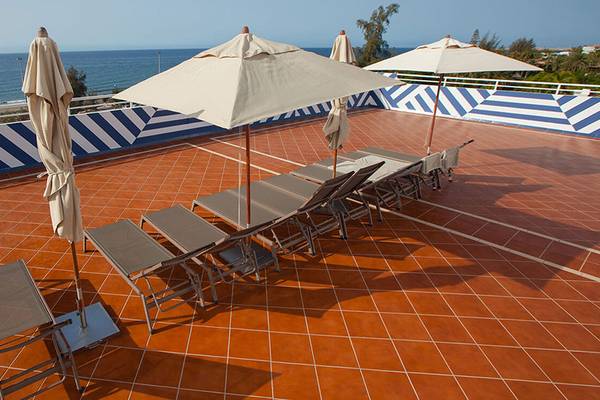 Terrasse des Corallium Beach by Lopesan Hotels mit Sonnenliegen und Sonnenschirmen.