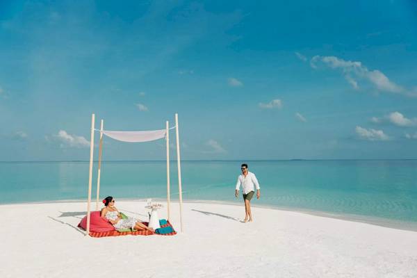 Nova Maldives Hotel Strand Sitzgelegenheit mit Sonnenschirm und Meer im Hintergrund.